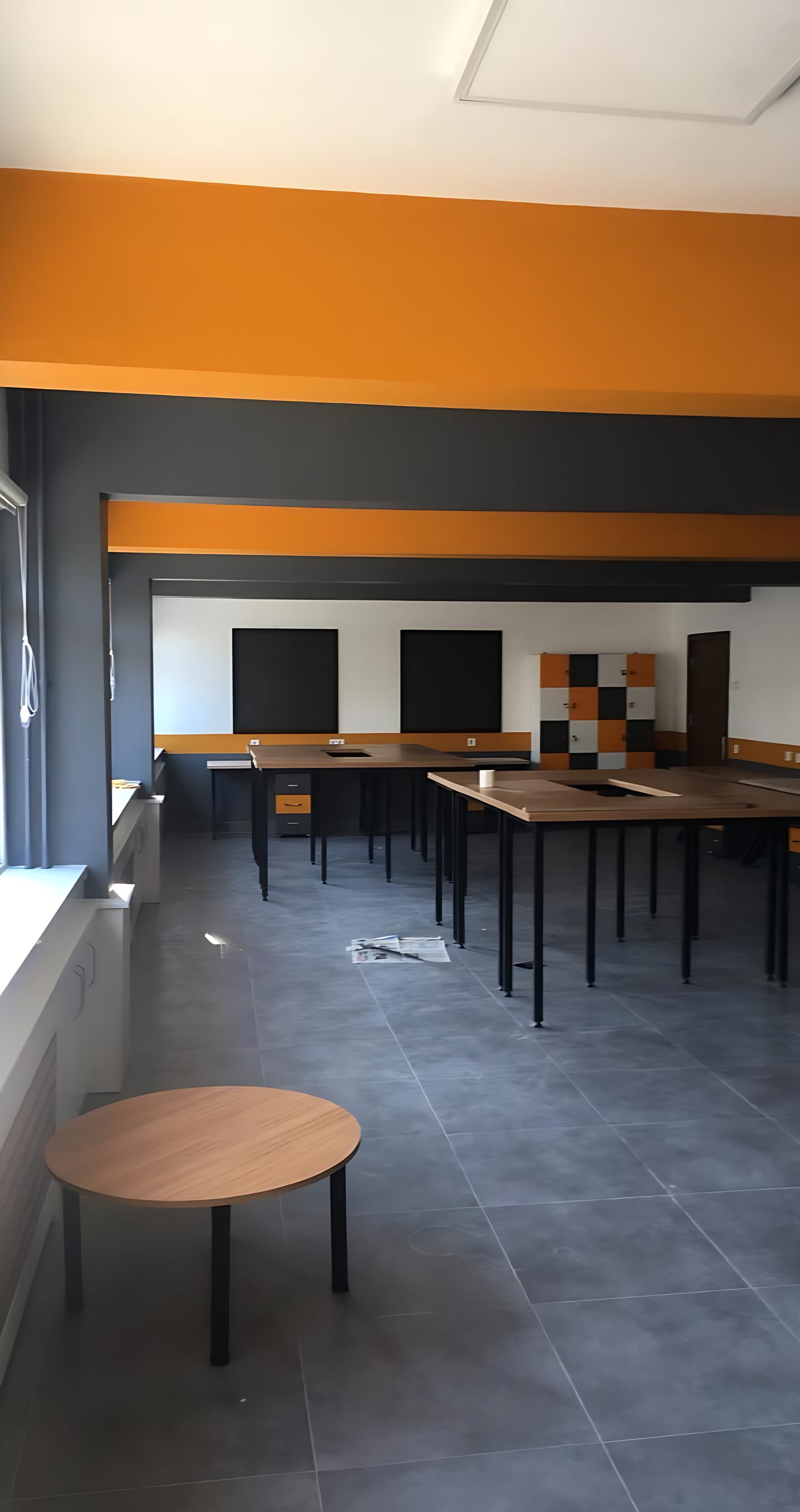 Turuncu bantlı duvar, renkli dolaplar ve çalışma masaları olan salon